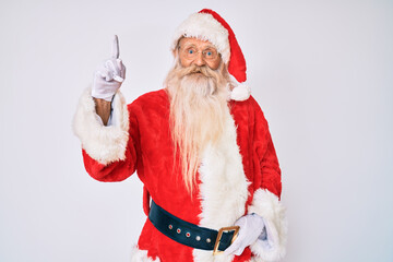 Old senior man with grey hair and long beard wearing santa claus costume with suspenders showing and pointing up with finger number one while smiling confident and happy.