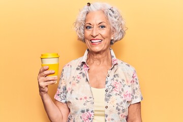 Senior grey-haired woman holding takeaway cup of coffee looking positive and happy standing and smiling with a confident smile showing teeth