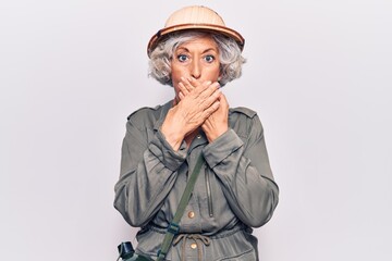 Senior grey-haired woman wearing explorer hat shocked covering mouth with hands for mistake. secret concept.
