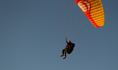 A beautiful view of a paraglide flying gliding on a clear blue sky at the golden hour with a nice wind windy breeze on a sunny day 