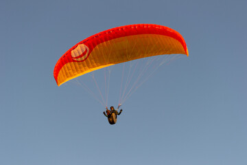 A beautiful view of a paraglide flying gliding on a clear blue sky at the golden hour with a nice wind windy breeze on a sunny day 