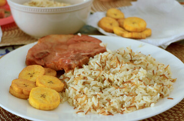 Rice with noodles, fried green plantains and fried pork chop.