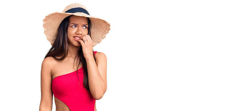 Young beautiful latin girl wearing swimwear and summer hat looking stressed and nervous with hands on mouth biting nails. anxiety problem.