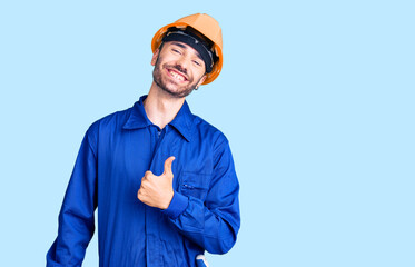 Young hispanic man wearing worker uniform doing happy thumbs up gesture with hand. approving expression looking at the camera showing success.