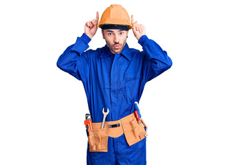 Young hispanic man wearing worker uniform doing funny gesture with finger over head as bull horns