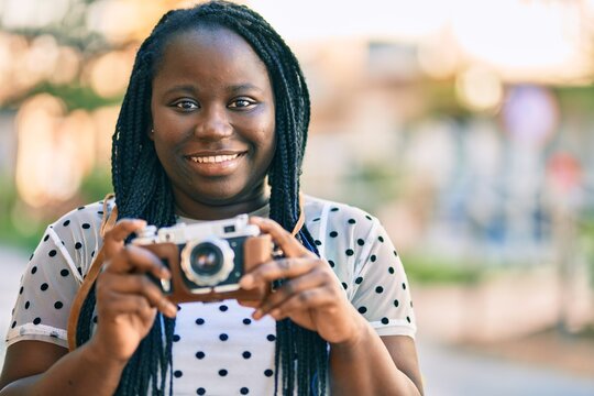 Young african american tourist woman smiling happy using vintage camera at the city.