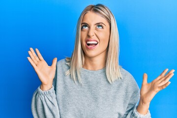 Beautiful blonde woman wearing casual clothes crazy and mad shouting and yelling with aggressive expression and arms raised. frustration concept.