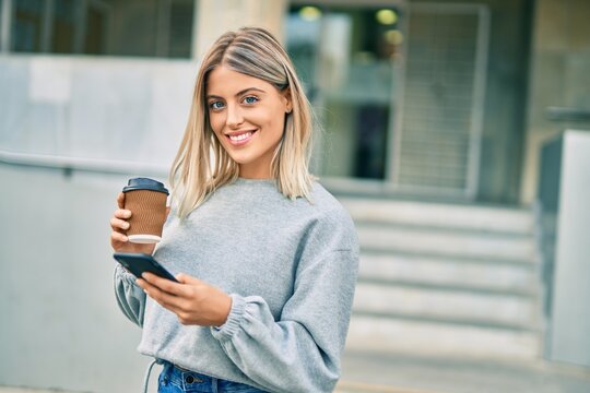 Young blonde girl using smartphone and drinking coffee at the city