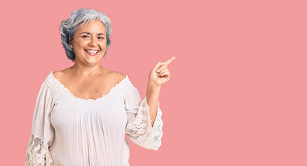 Senior woman with gray hair wearing bohemian style with a big smile on face, pointing with hand finger to the side looking at the camera.