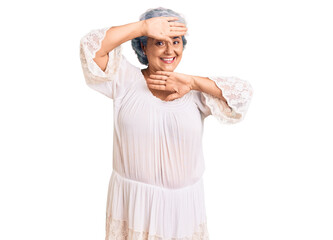 Senior woman with gray hair wearing bohemian style smiling cheerful playing peek a boo with hands showing face. surprised and exited