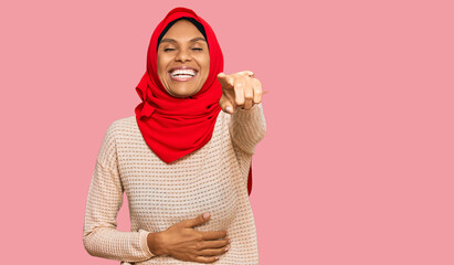 Young african american woman wearing traditional islamic hijab scarf laughing at you, pointing finger to the camera with hand over body, shame expression