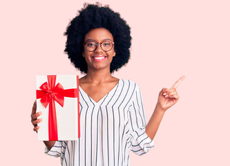 Young african american woman holding gift smiling happy pointing with hand and finger to the side