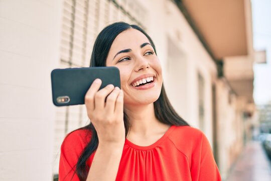 Young latin girl smiling happy sending voice message using smartphone at the city.