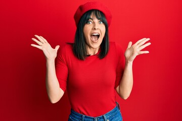 Young hispanic woman wearing french look with beret celebrating crazy and amazed for success with arms raised and open eyes screaming excited. winner concept