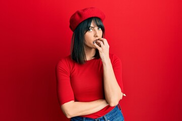 Naklejka premium Young hispanic woman wearing french look with beret looking stressed and nervous with hands on mouth biting nails. anxiety problem.
