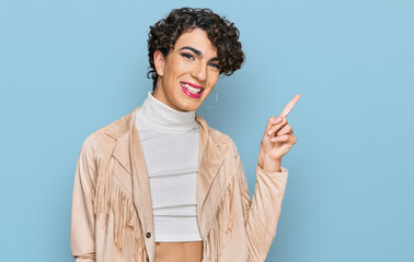 Handsome man wearing make up and woman clothes with a big smile on face, pointing with hand finger to the side looking at the camera.