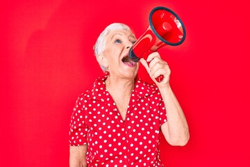 Senior beautiful grey-haired woman screaming using megaphone over isolated red background