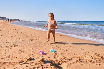 Fototapeta na wymiar Adorable blonde child wearing bikini. Building sand castle using bucket and shovel at the beach