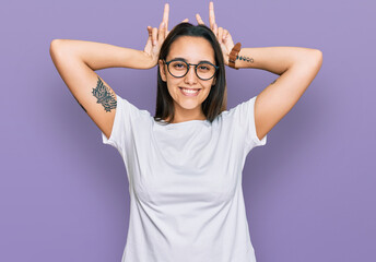 Obraz na płótnie Canvas Young hispanic woman wearing casual white t shirt posing funny and crazy with fingers on head as bunny ears, smiling cheerful