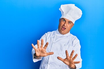 Mature middle east man wearing professional cook uniform and hat afraid and terrified with fear...