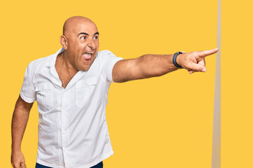 Mature middle east man with mustache wearing casual white shirt pointing with finger surprised ahead, open mouth amazed expression, something on the front