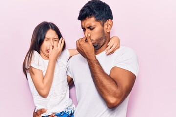 Young father and daughter wearing casual clothes smelling something stinky and disgusting,...