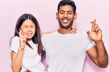 Young father and daughter wearing casual clothes gesturing finger crossed smiling with hope and eyes closed. luck and superstitious concept.