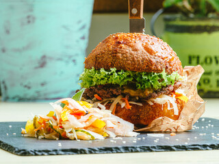 fresh tasty burger and French fries Side view closeup of a burger with a rye dark bun on the black pan on the wooden table dark background, horizontal