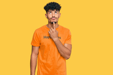 Young arab man wearing tshirt with happiness word message thinking concentrated about doubt with...