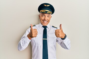 Handsome middle age mature man wearing airplane pilot uniform success sign doing positive gesture...