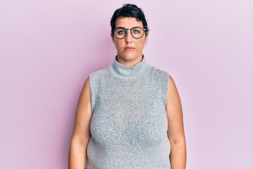 Plus size brunette woman wearing casual clothes and glasses with serious expression on face. simple...
