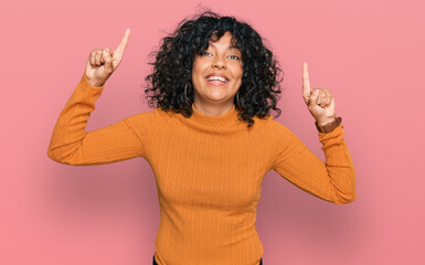 Young hispanic woman wearing casual clothes smiling amazed and surprised and pointing up with fingers and raised arms.