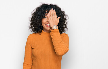 Young hispanic woman wearing casual clothes covering one eye with hand, confident smile on face and surprise emotion.