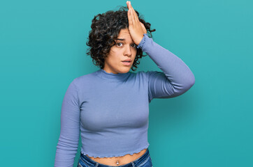 Young hispanic woman with curly hair wearing casual clothes surprised with hand on head for...