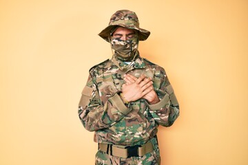 Young handsome man wearing camouflage army uniform and balaclava smiling with hands on chest with closed eyes and grateful gesture on face. health concept.