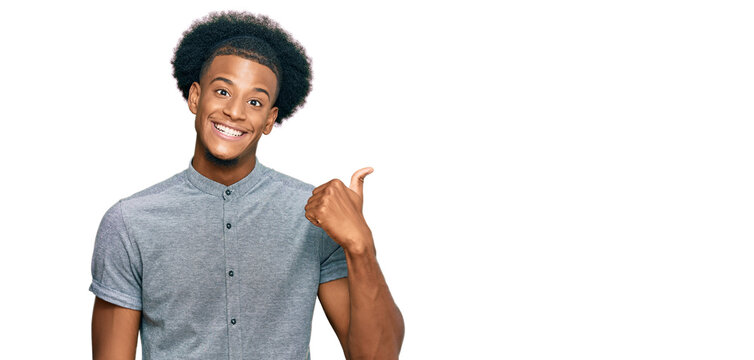 African american man with afro hair wearing casual clothes smiling with happy face looking and pointing to the side with thumb up.
