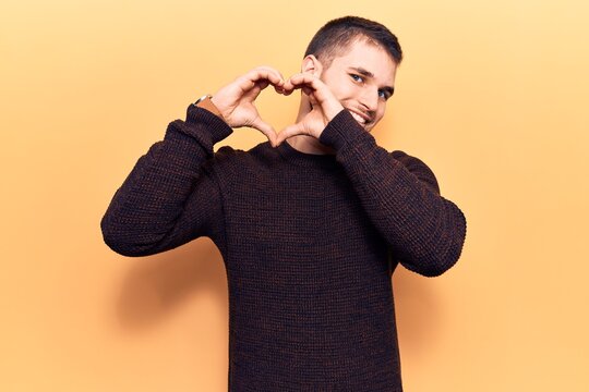 Young handsome man wearing casual sweater smiling in love doing heart symbol shape with hands. romantic concept.
