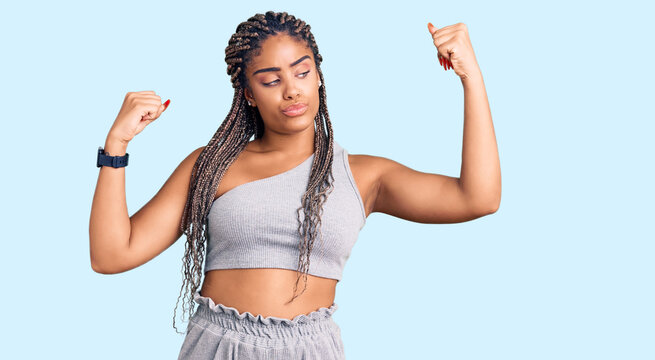 Young african american woman with braids wearing sportswear showing arms muscles smiling proud. fitness concept.