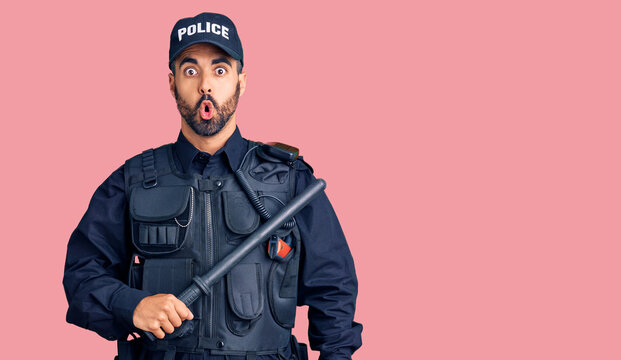 Young hispanic man wearing police uniform holding baton scared and amazed with open mouth for surprise, disbelief face