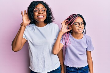 Fototapeta na wymiar Beautiful african american mother and daughter wearing casual clothes and glasses smiling with hand over ear listening an hearing to rumor or gossip. deafness concept.
