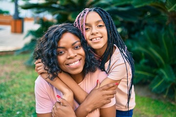 Naklejka premium Beautiful african american mother and daughter smiling happy and hugging. Standing with smile on face standing at the park.