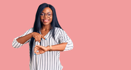 Young african american woman wearing casual clothes and glasses in hurry pointing to watch time,...