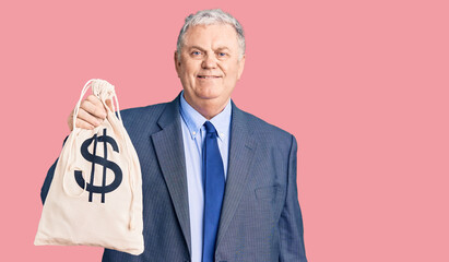 Senior grey-haired man wearing business suit holding money bag with dollar symbol looking positive...