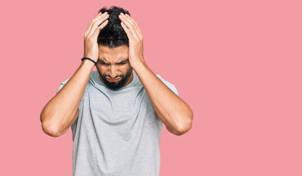 Young man with beard wearing casual grey tshirt suffering from headache desperate and stressed because pain and migraine. hands on head.