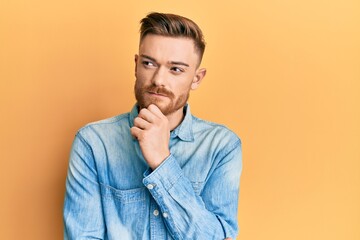 Young redhead man wearing casual denim shirt thinking concentrated about doubt with finger on chin and looking up wondering