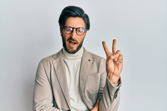Young hispanic man wearing business jacket and glasses smiling with happy face winking at the camera doing victory sign. number two.