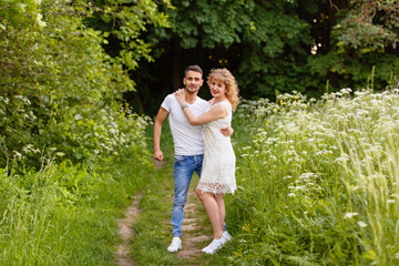 Young man and woman couple walk in the meadow. Tender holding each other. Spring lovestory. Blonde-haired girl with curled hairs and man weared in casual and denim. Young family