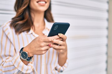 Young hispanic woman smiling happy using smartphone at the city.
