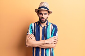 Young handsome man with beard wearing summer hat and shirt skeptic and nervous, disapproving expression on face with crossed arms. negative person.