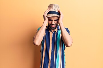 Young handsome man with beard wearing summer hat and shirt suffering from headache desperate and stressed because pain and migraine. hands on head.